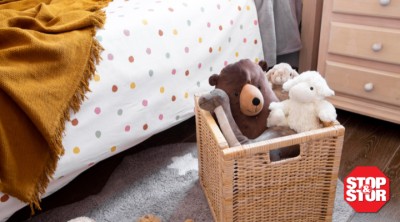 A woven storage basket filled with stuffed animals beside a child’s bed, demonstrating a simple and tidy storage solution for organizing kids’ toys in a family home.
