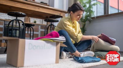 A person sitting on the floor sorting and folding clothes into a donation box in a bright, cozy living space, illustrating the process of decluttering and organizing belongings.