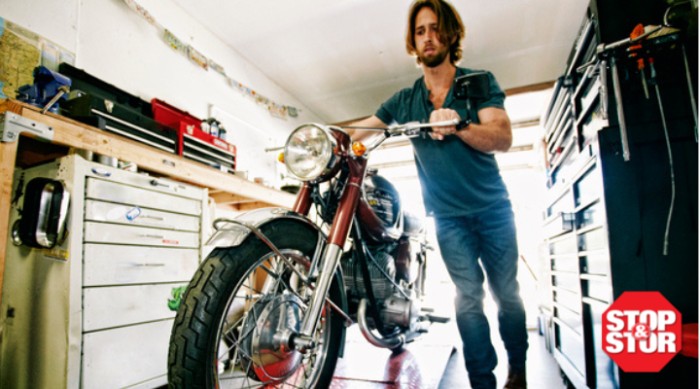 man pushes motorcycle up a ramp into motorcycle shop for repair